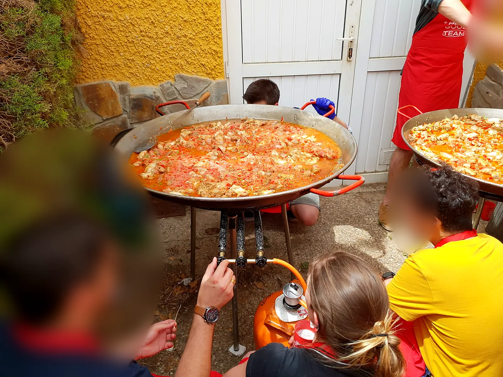 Equipo de un team building alrededor de su paella mientras ajusta el fuego de gas